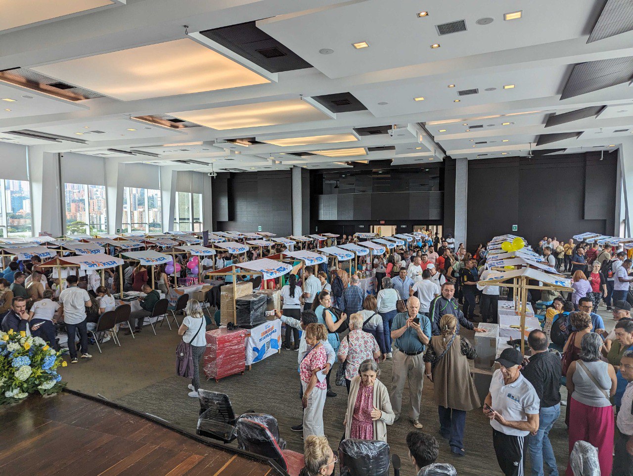 La revente d’importation transfrontalière EC est un événement intérieur de grande envergure, où un grand nombre de personnes se tiennent debout et discutent autour d’une table, avec une variété d’objets exposés dans une salle aux grandes fenêtres et avec vue sur la ville.